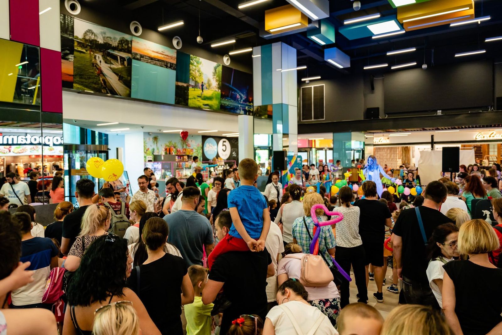 Sute de părinți și copii adunați în food court-ul centrului comercial la un spectacol