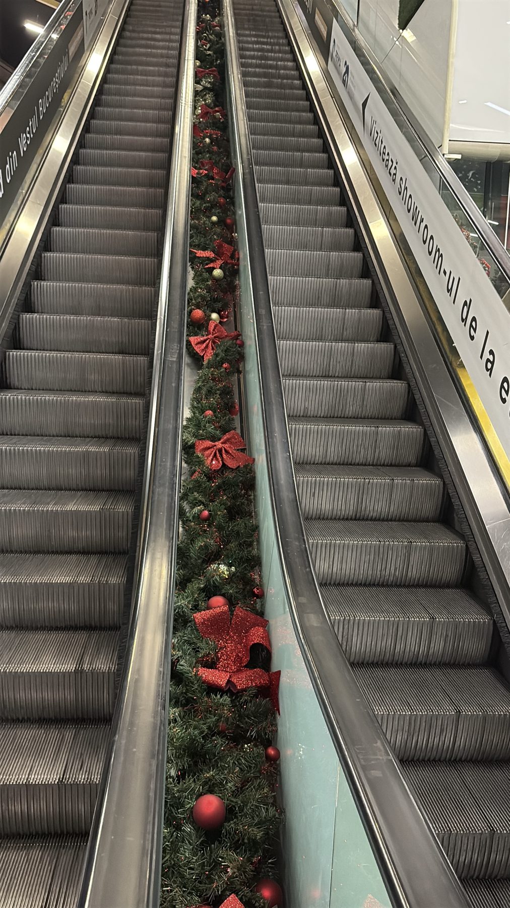 Ghirlandă de brad cu funde roșii între scările rulante